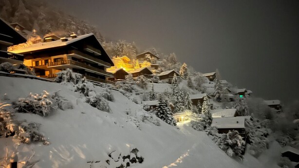 A snow-covered mountain village with illuminated buildings and a ski lift.