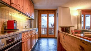 A kitchen with wooden cabinets, a red coffee machine, and a view of mountains through the door.