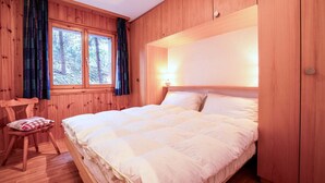 A wooden-paneled bedroom with a large bed, a chair, and a window with curtains.