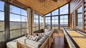 A log cabin with a large window overlooking a mountainous landscape, a wooden ceiling fan, and a cozy seating area with cushions. - Scenic Views•Hot Tub•Near Downtown (Gatlinburg)