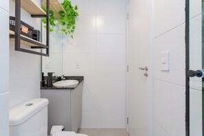 A modern bathroom with a toilet, sink, and a mirror. - New Life Visconde - Yogha (Curitiba)