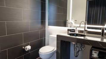 A modern bathroom with dark tiles, a white toilet, a sink with a mirror, and a makeup station.