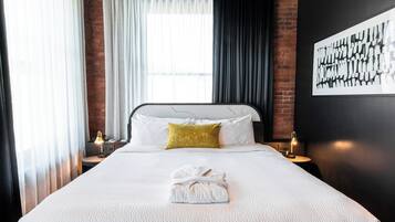 A hotel room with a large bed, a white comforter, a gold throw pillow, a neatly folded towel, and a black and white abstract painting on the wall.