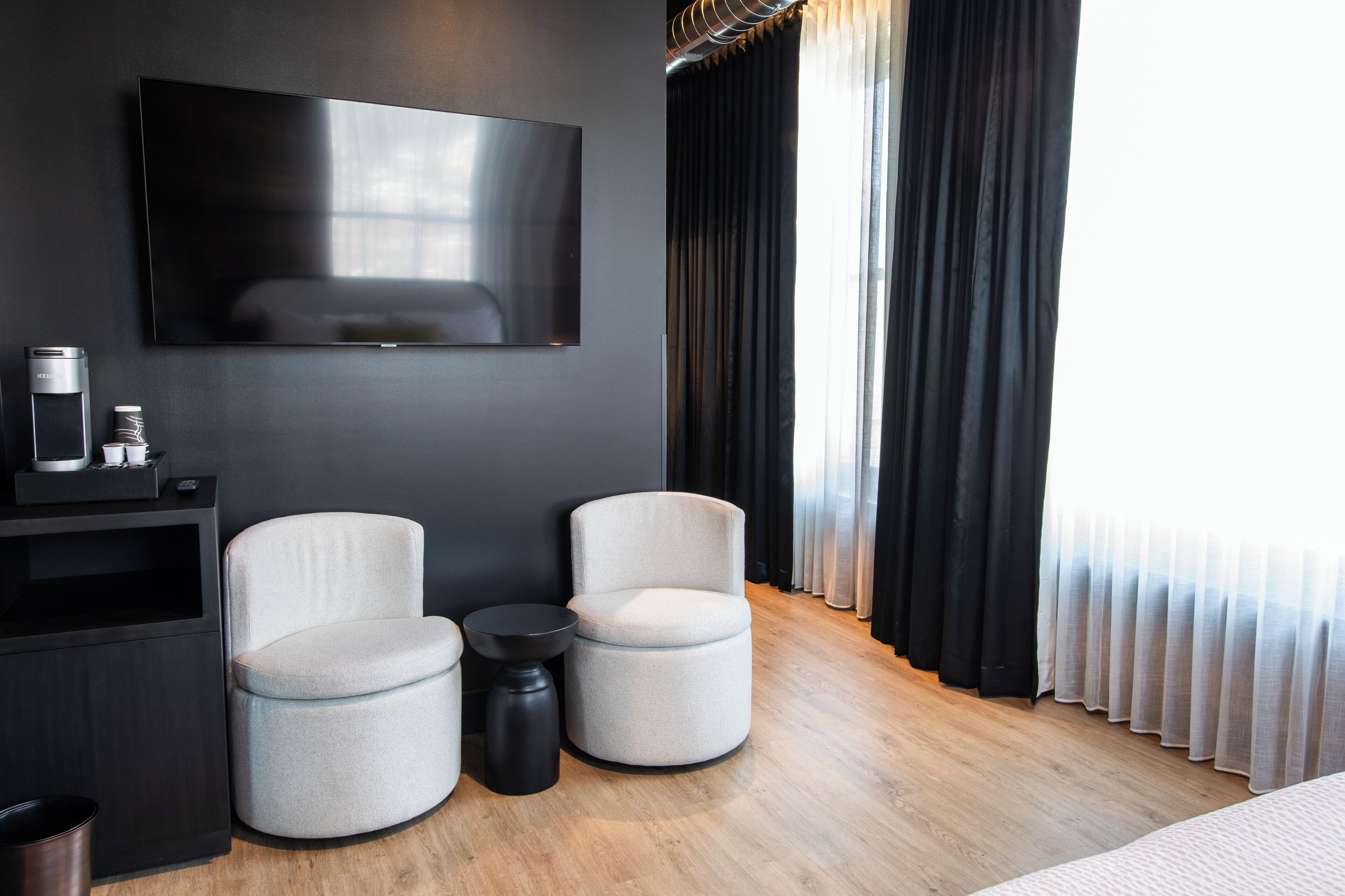 A modern hotel room with a flat-screen TV, two armchairs, a small side table, and a coffee machine.
