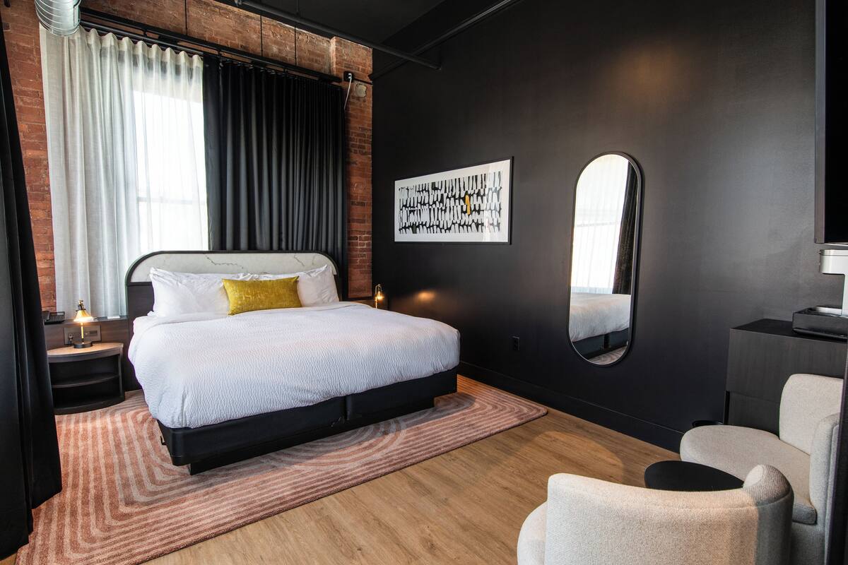Un dormitorio moderno con una cama grande, un espejo redondo y una obra de arte en la pared.