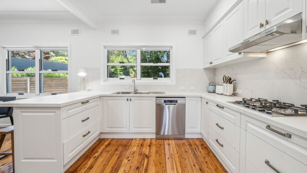 Una cocina moderna con armarios blancos, un lavavajillas de acero inoxidable y una cocina a gas.