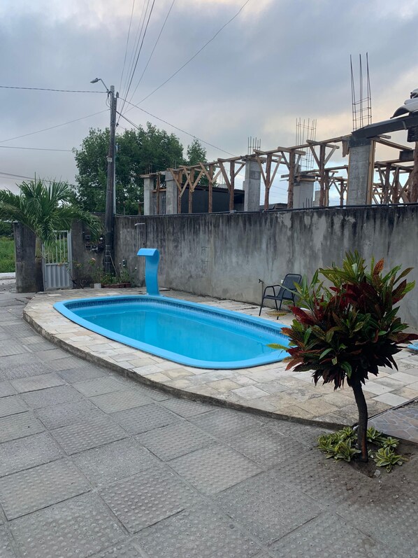 A swimming pool with a concrete deck, surrounded by a low wall and a wooden structure in the background. - Flat 201 proximo centro Porto de Galinha (Ipojuca)