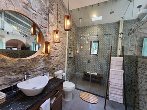 A modern bathroom with a stone wall, a large mirror, a sink, and a glass shower enclosure. - Castello di Carlo - Suite Carlo V (Val'Quirico)
