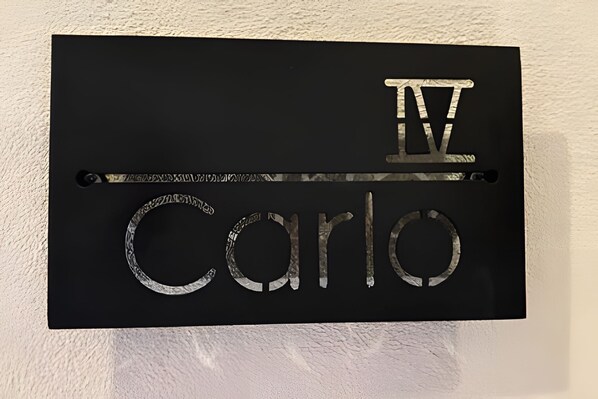 A black sign with the name "IV Carlos" in metallic letters. - Castello di Carlo - Suite Carlo IV (Val'Quirico)