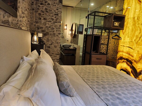 A bedroom with a stone wall, a bed with white linens, a wooden dresser, and a mirror.