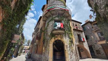 A narrow cobblestone street flanked by historic stone buildings with balconies, some adorned with flags.