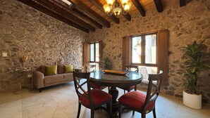 Una habitación de paredes de piedra con una mesa redonda, sillas tapizadas en rojo, un sofá y una araña.