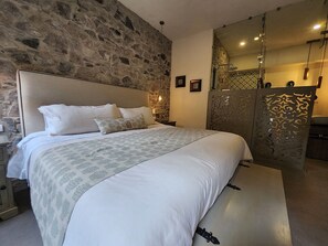 A bedroom with a stone wall, a bed with white bedding, a nightstand, and a mirror with a decorative panel. - Castello di Carlo - Loft Carlo III (Val'Quirico)