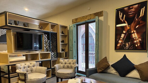 Una sala de estar moderna con un sofá, dos sillones, una mesa de centro con un libro, un televisor y una estantería.