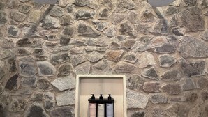 A stone wall with a shelf holding two bottles of OAN body wash and conditioner. - Castello di Carlo – Loft Carlo II (Val'Quirico)
