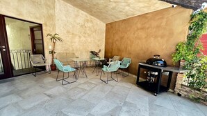 Eine Terrasse im Freien mit Tisch, Stühlen, einem Grill und Topfpflanzen.
