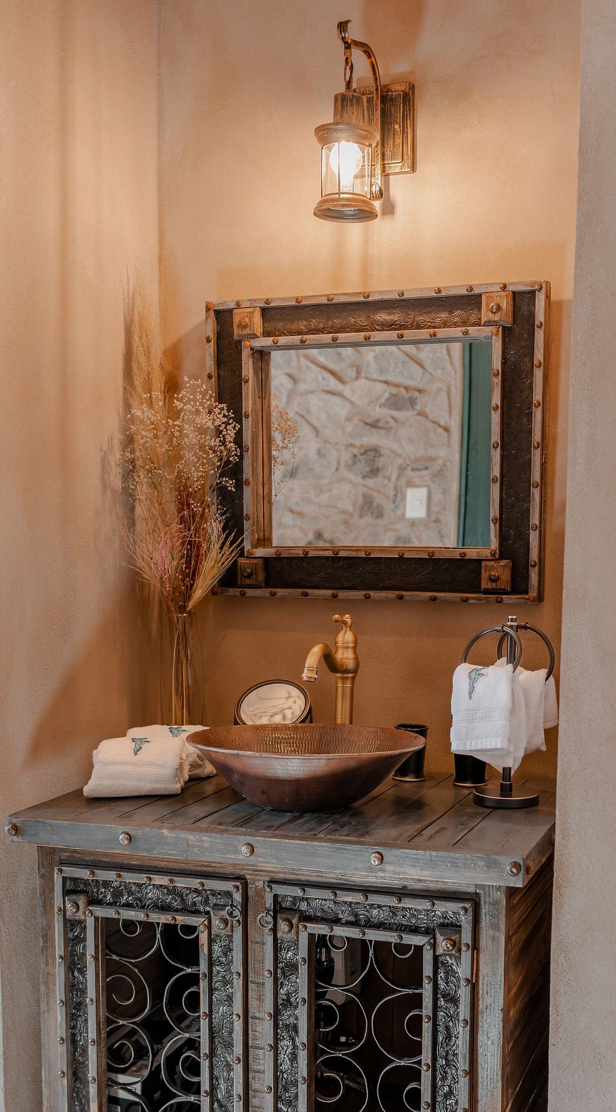 Un baño rústico con un lavamanos antiguo, un espejo colgado en la pared y una lámpara decorativa.