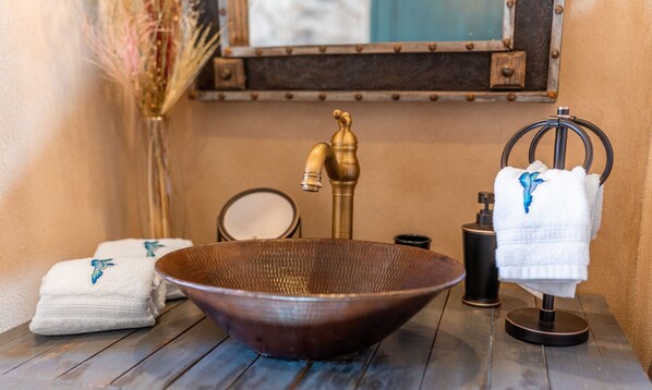 A bathroom with a wooden bowl sink, a brass faucet, a mirror, a towel rack, and a decorative vase.