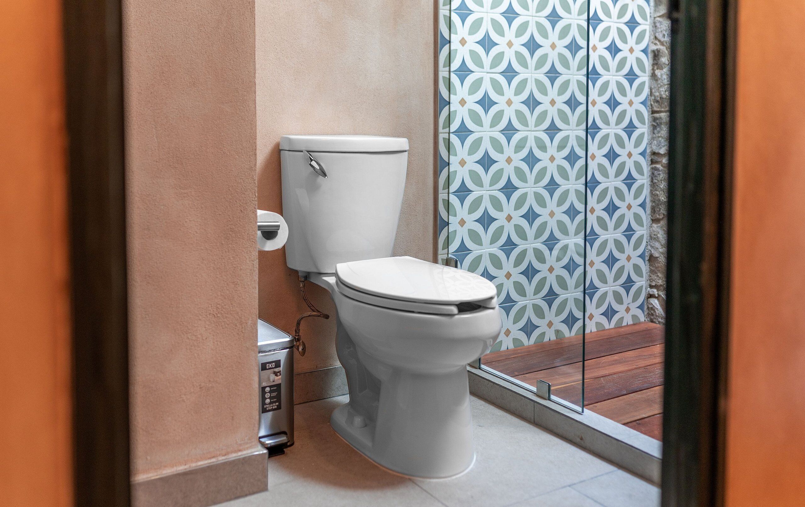 A modern bathroom with a white toilet, a wall-mounted bidet, and a patterned tile backsplash.
