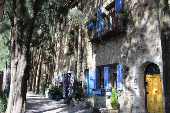 Un edificio de piedra con contraventanas azules, una puerta amarilla y plantas en macetas.