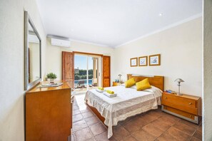 A bedroom with a bed, bedside table, lamp, and a view of a swimming pool through an open door. - Villa Casa Brasil by Villa Plus (Praia do Carvoeiro)