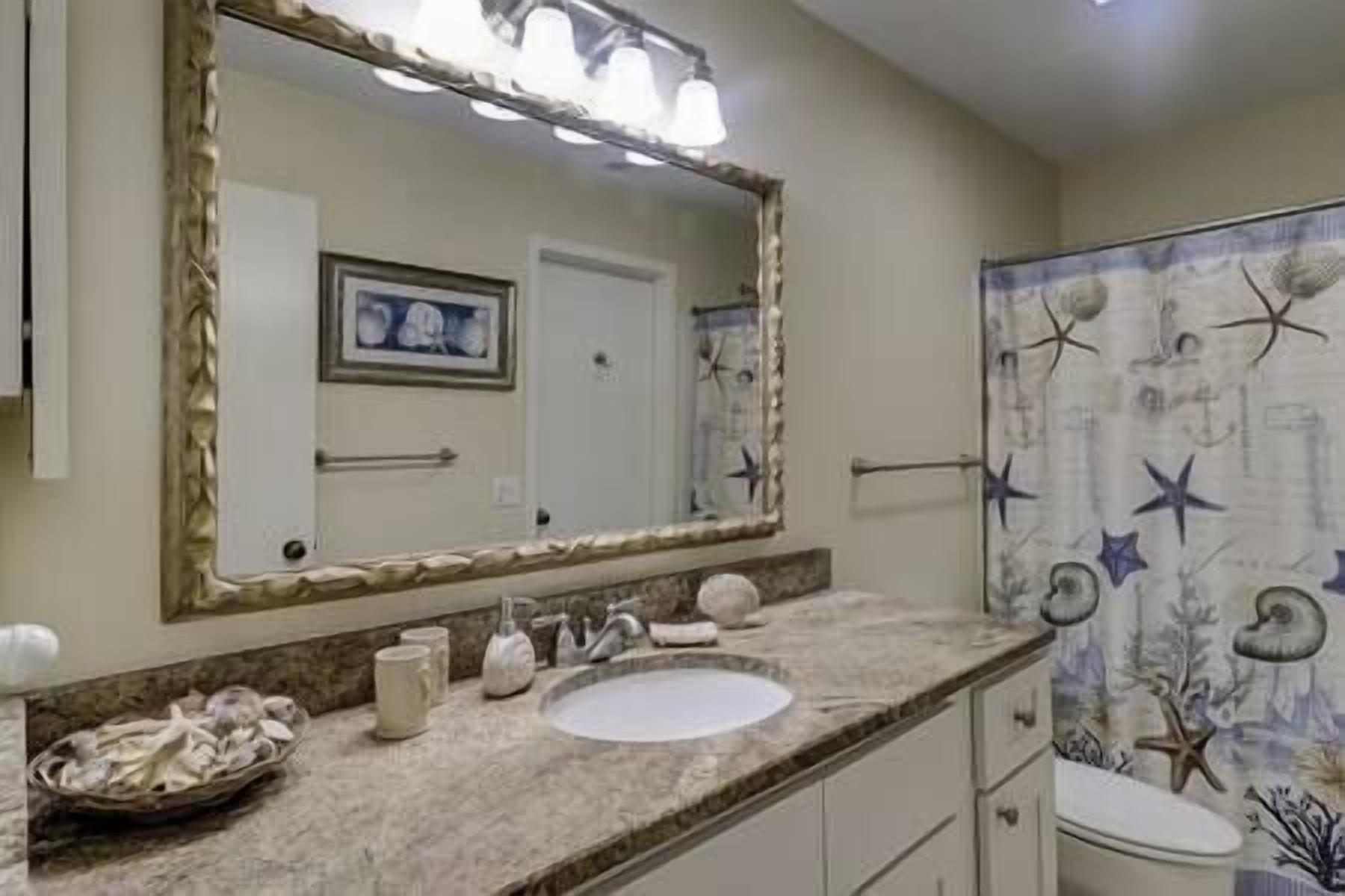A bathroom with a large mirror, a sink, a towel rack, and a shower curtain with a starfish pattern.