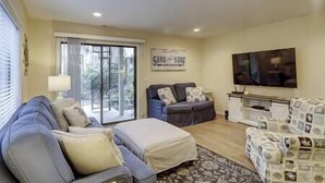 A living room with a sofa, a coffee table, a TV, and a sliding glass door leading to a balcony. - 13Beach Stop Hilton Head (Hilton Head Island)