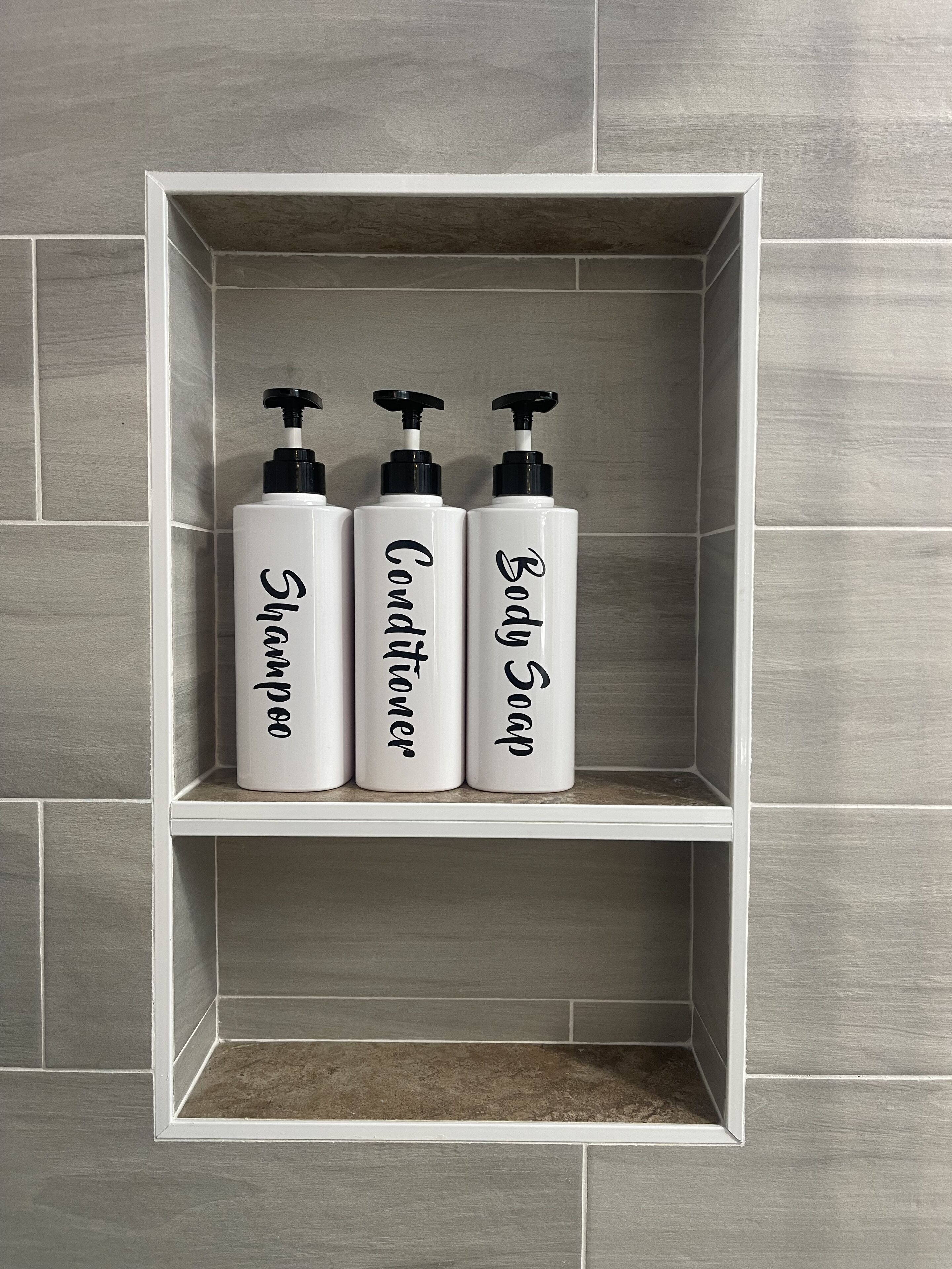 A bathroom shelf with three bottles labeled shampoo, conditioner, and body soap.
