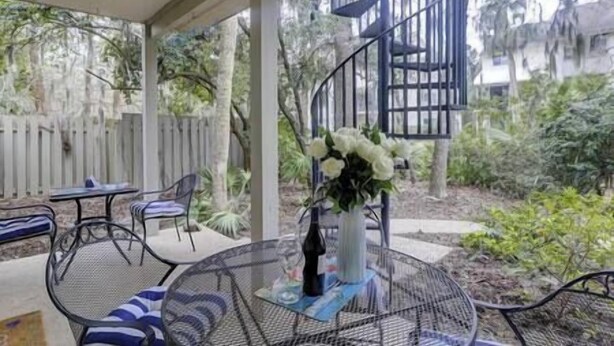 A covered patio area with a spiral staircase, outdoor seating, and a flower arrangement. - 13Beach Stop Hilton Head (Hilton Head Island)