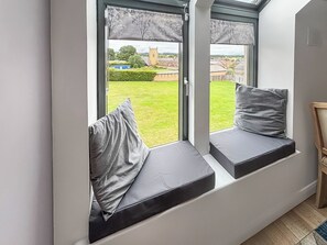A room with a built-in bench seat by a window overlooking a green lawn and a distant building. - 1 bedroom accommodation in Alnwick (Alnwick)