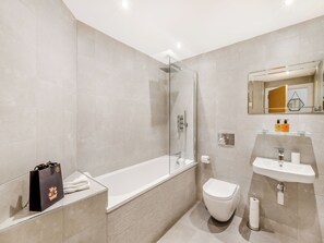 Un baño moderno con ducha de vidrio, una bañera blanca, un inodoro blanco y un lavabo con espejo.