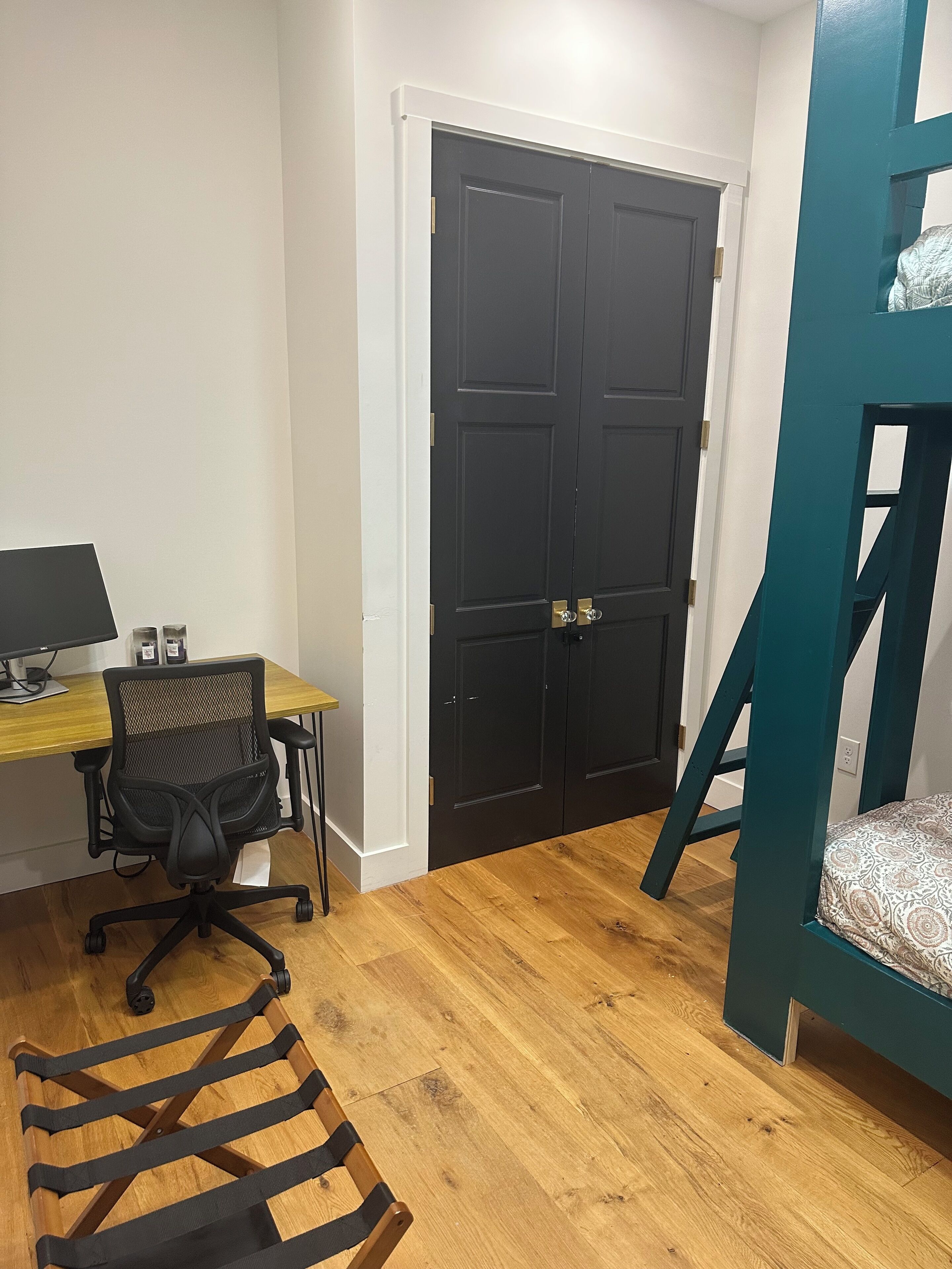 A room with a desk, computer, chair, bunk bed, and a door.