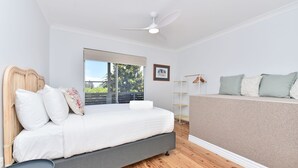 A bedroom with a bed, a standing fan, a window with a view, and a framed picture on the wall. - Living The Dream Soldiers Point Home with BBQ (Soldiers Point)