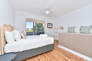 Een slaapkamer met een bed, een ventilator, een raam met uitzicht en een ingelijst beeld aan de muur.