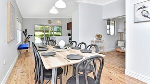 A modern dining area with a wooden table set for six, surrounded by black chairs. - Living The Dream Soldiers Point Home with BBQ (Soldiers Point)