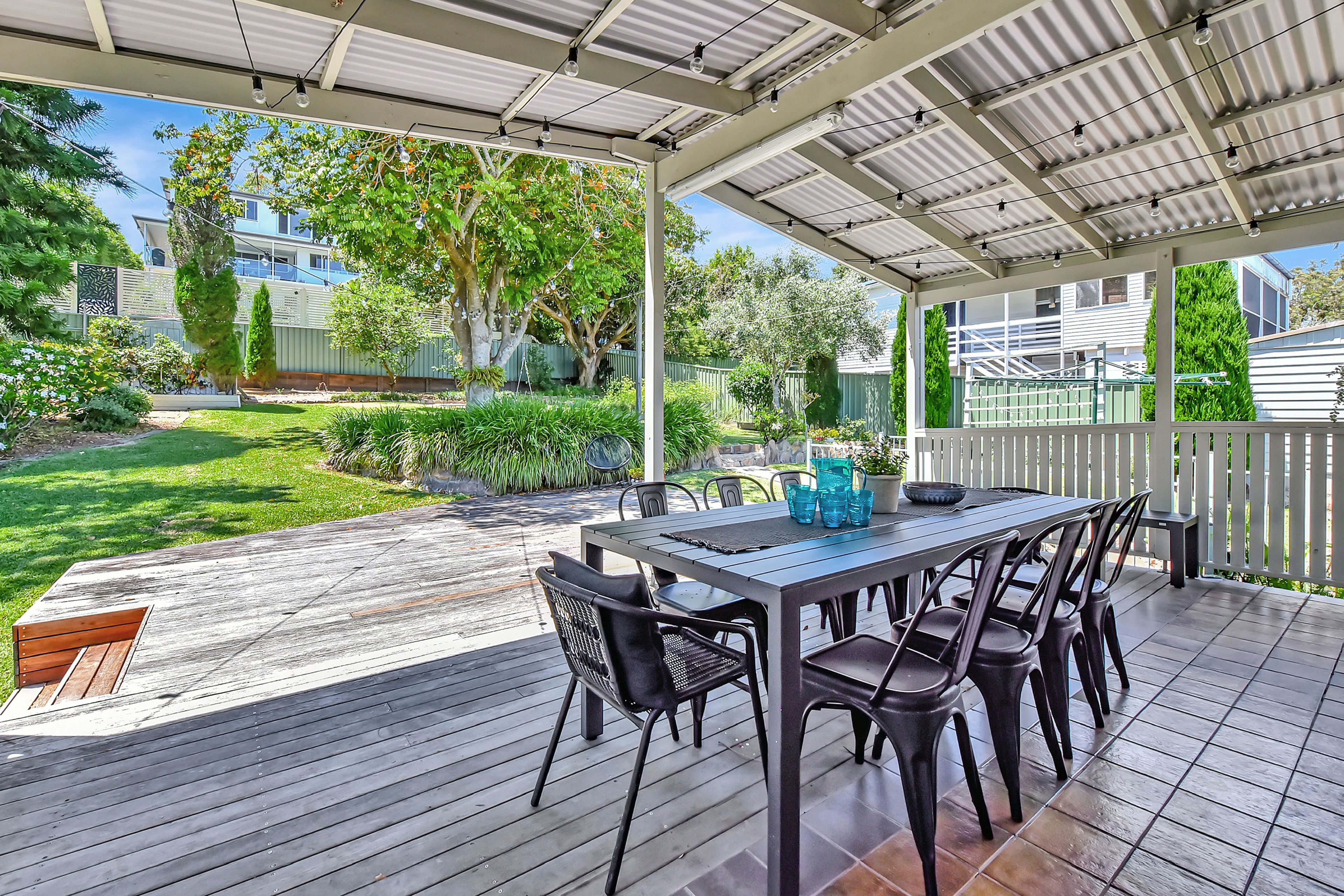 Eine Terrasse im Freien mit Tisch und Stühlen, umgeben von einer Holzterrasse und einem überdachten Bereich mit Metalldach.
