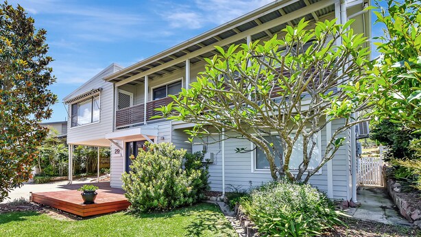 A two-story house with a covered porch, a small garden, and a tree in the front yard. - Living The Dream Soldiers Point Home with BBQ (Soldiers Point)