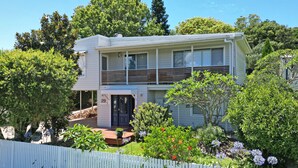 A two-story house with a balcony, surrounded by lush greenery and a white picket fence. - Living The Dream Soldiers Point Home with BBQ (Soldiers Point)