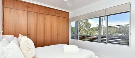 A bedroom with a bed, wooden wardrobe, ceiling fan, and a window with a view of trees.