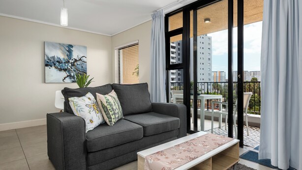 Ein modernes Wohnzimmer mit einem grauen Sofa, einem Couchtisch und einem großen Fenster mit Blick auf Gebäude.