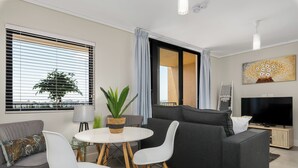 Ein modernes Wohnzimmer mit einem grauen Sofa, weißen Sesseln, einem kleinen runden Tisch und einem Fernseher.
