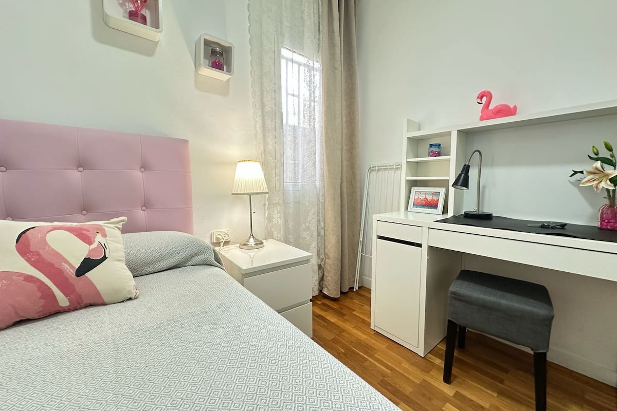 Une chambre bien rangée, avec un lit, une table de chevet, un bureau, une chaise et une fenêtre avec des rideaux.