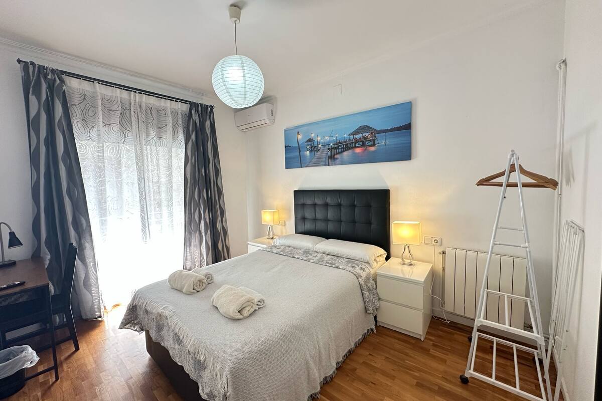 Une chambre bien rangée, avec un lit, des tables de chevet, un luminaire suspendu, un radiateur et un tableau au mur.