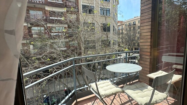 Un balcon avec une table et deux chaises, donnant sur un paysage urbain avec des immeubles et des arbres.