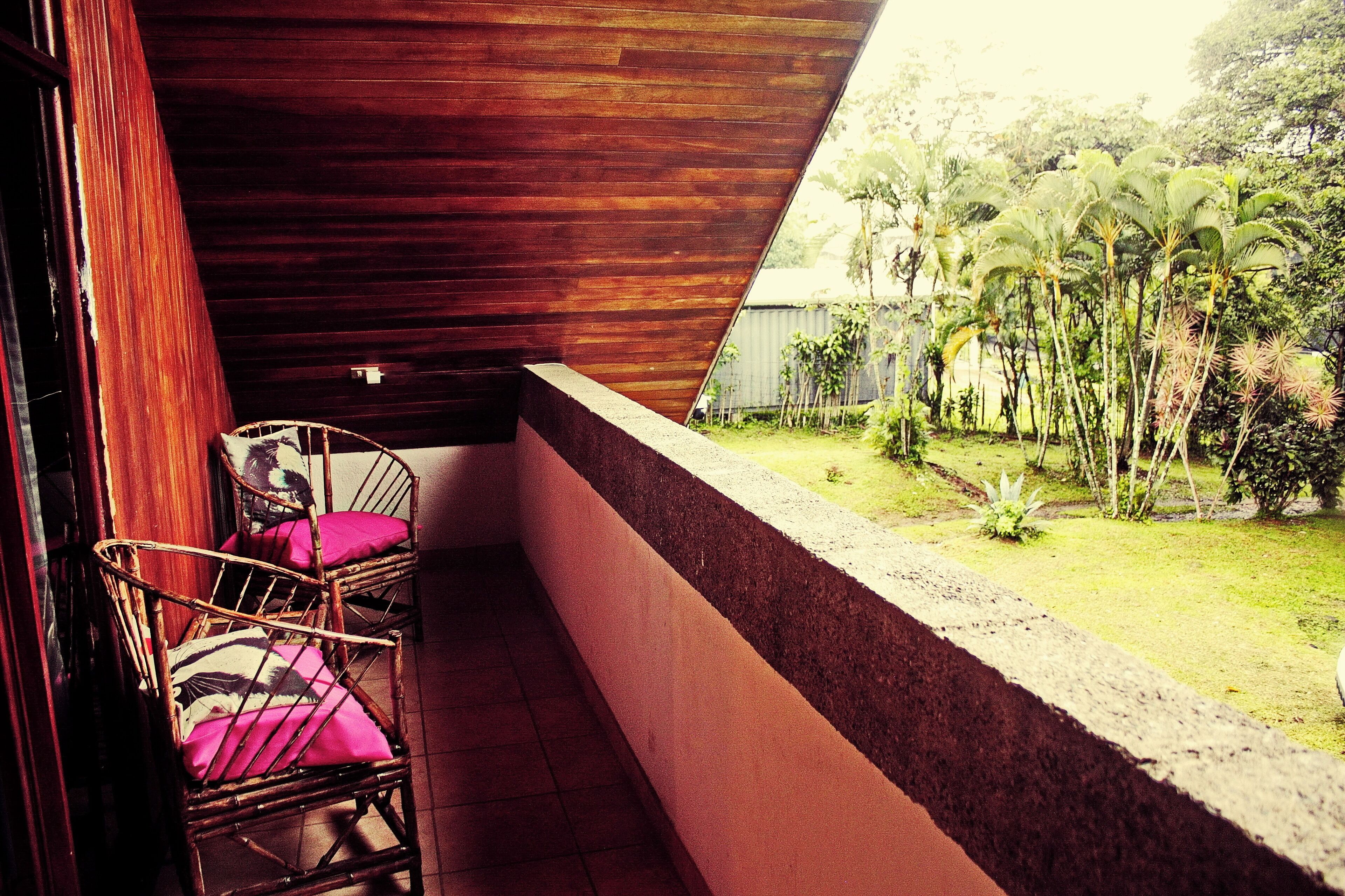 A balcony with two wicker chairs and a view of a garden with various plants.