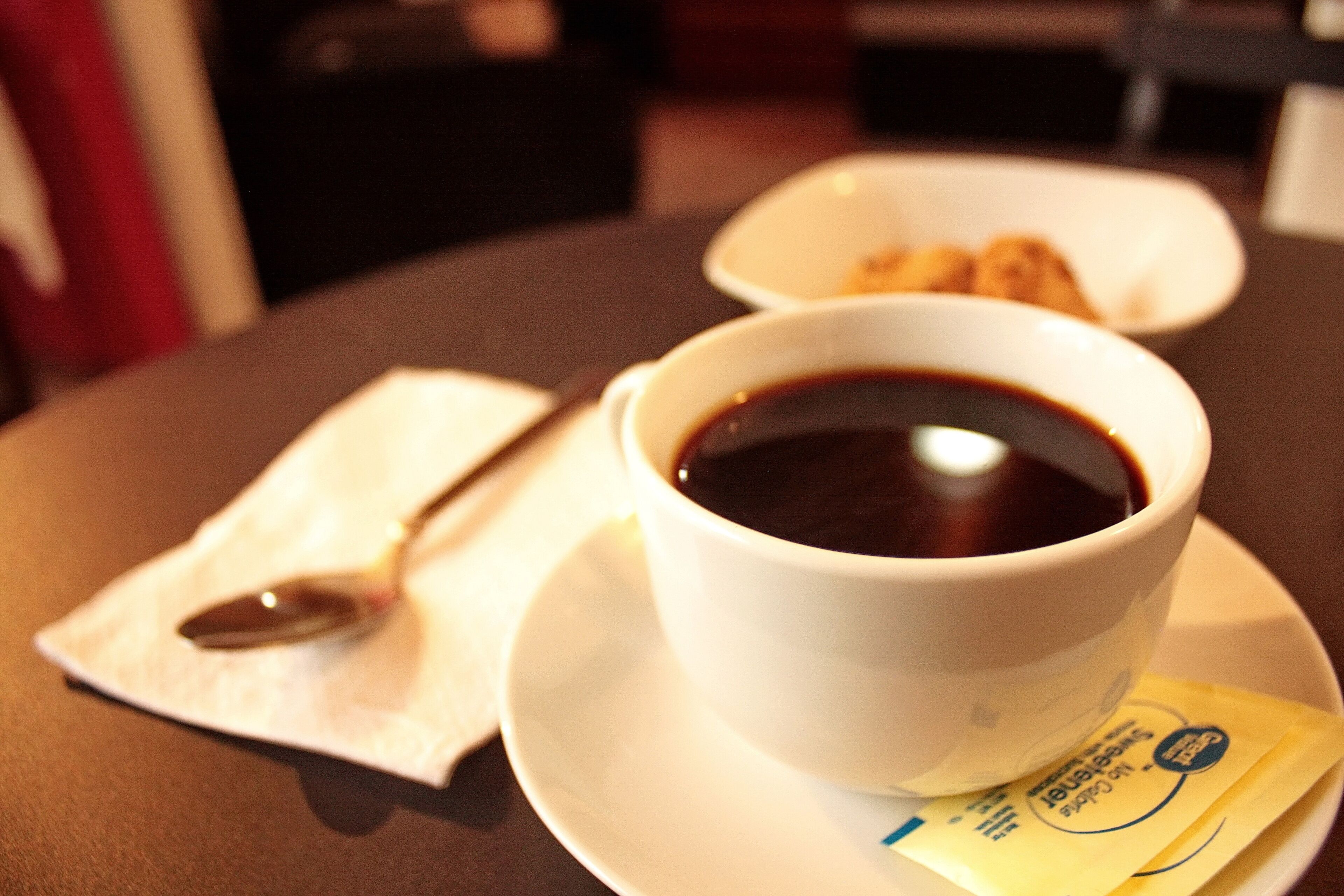 A cup of coffee on a saucer with a spoon and a packet of creamer on a table.