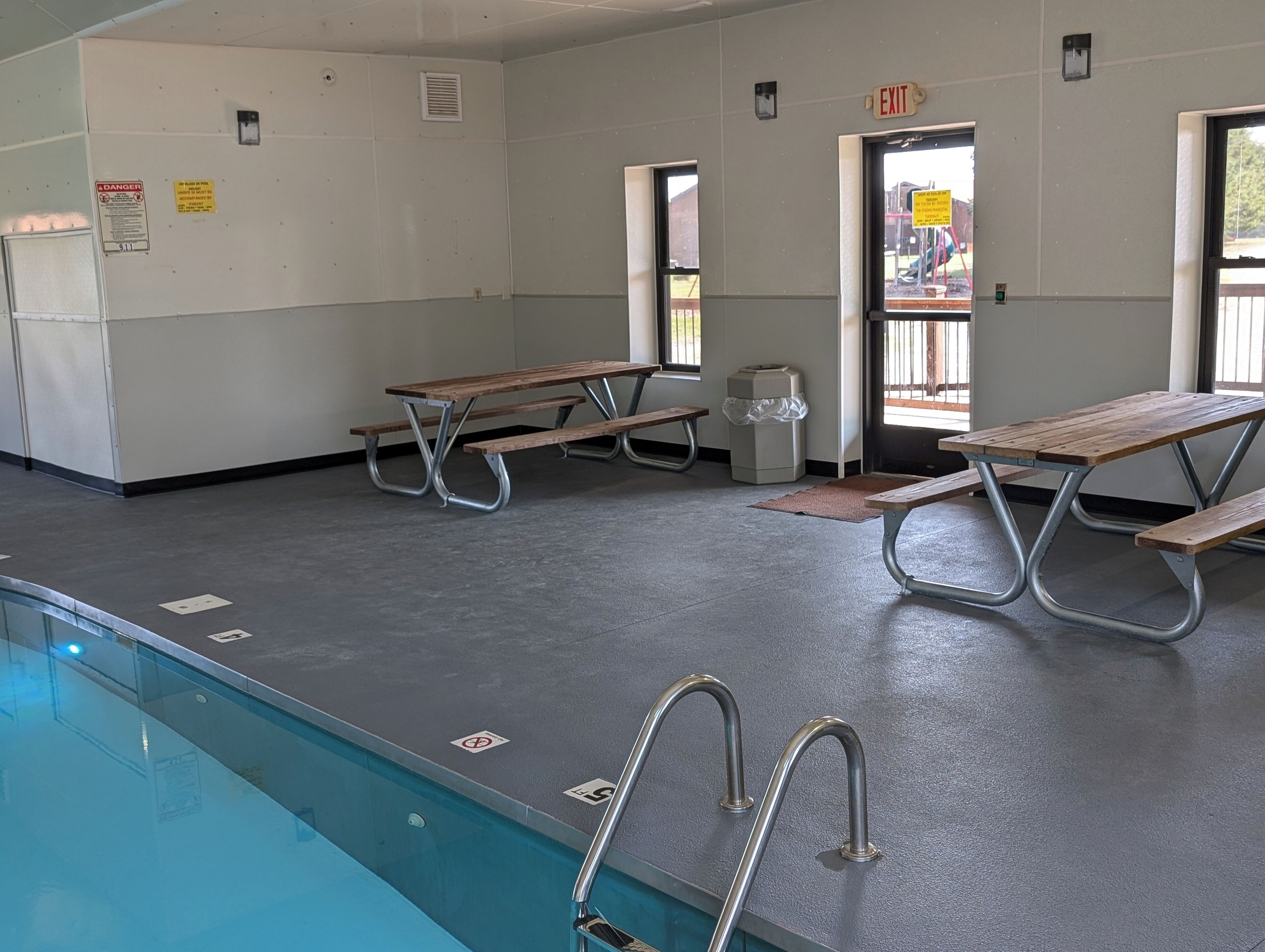 Zona de piscina con mesas de picnic y un cubo de basura.