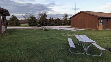 A grassy outdoor area with picnic tables and a shed.