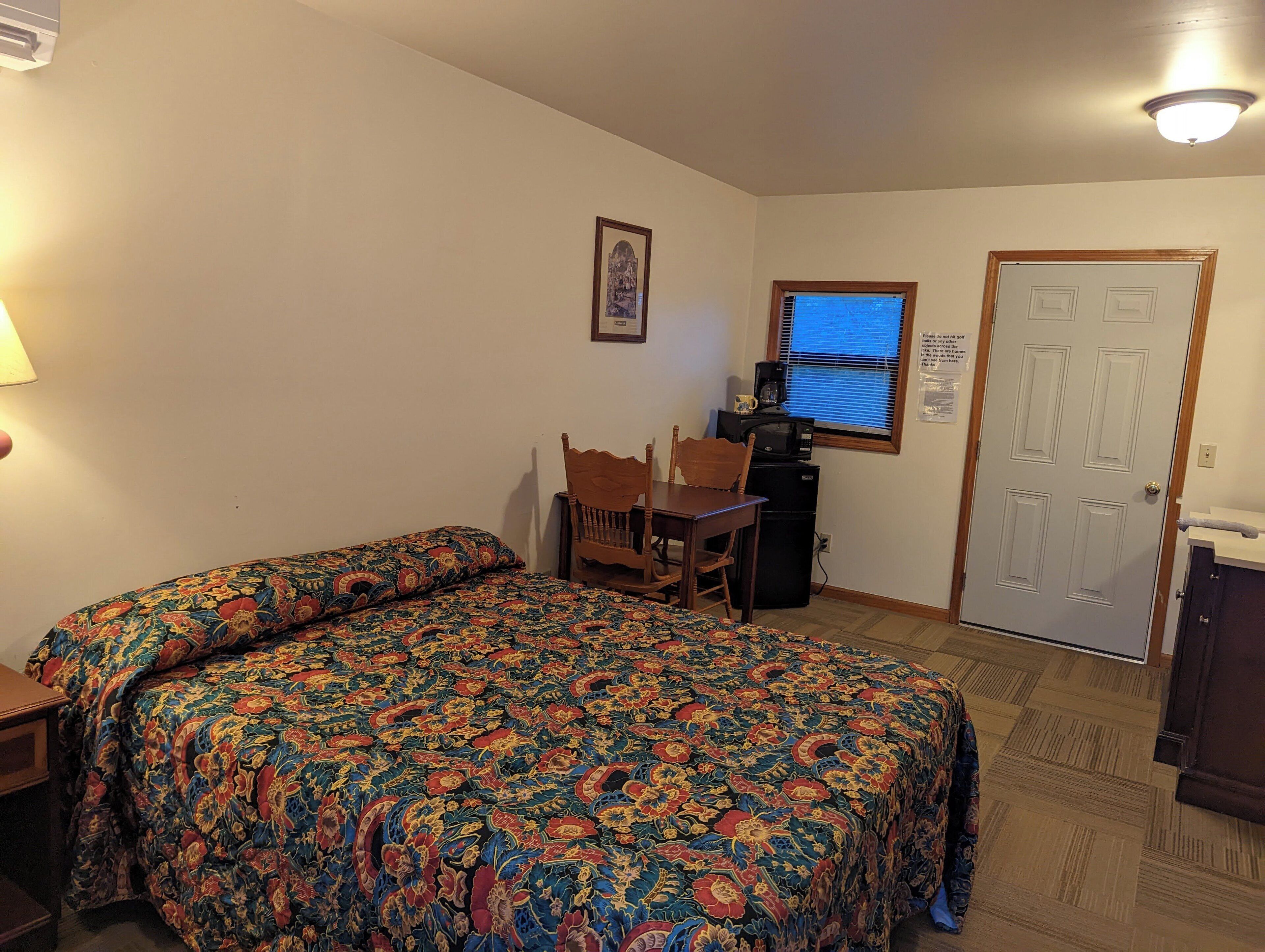 A room with a bed, a desk with a chair, a microwave, and a door.