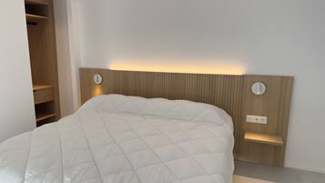 A bed with a quilted white duvet, a wooden headboard with vertical slats, and two wall-mounted light fixtures.